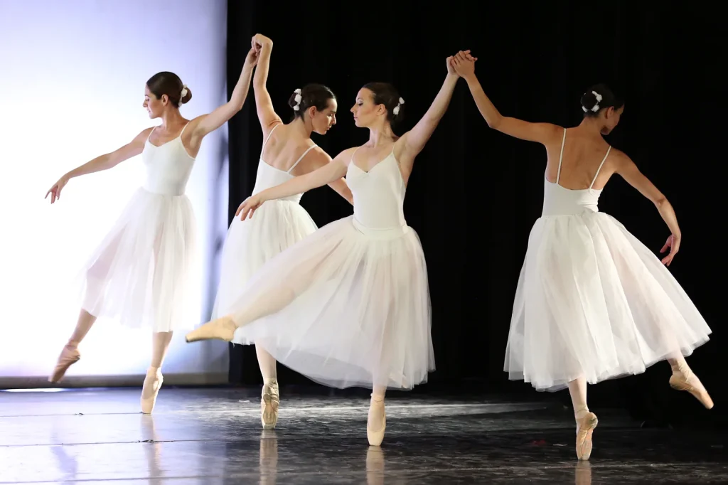 Cuatro bailarinas de blanco con las manos unidas en el festival de CDAM