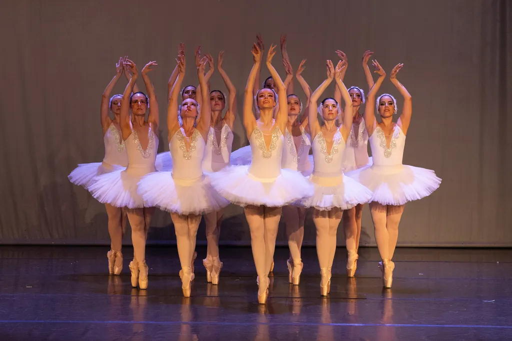 Cuerpo de baile con tutús blancos y brazos en alto en el Festival de Fin de Curso de CDAM