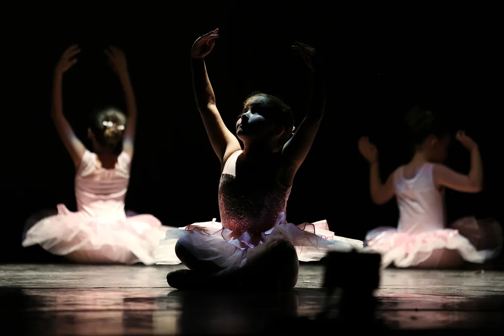 Alumnas de ballet infantil sentadas en escena con los brazos en alto en el Festival de CDAM