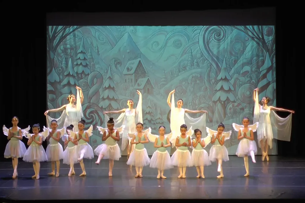 Niñas vestidas de ángel con alas y tutú blanco, y bailarinas con velos detrás, en el segundo acto de El Cascanueces de la escuela